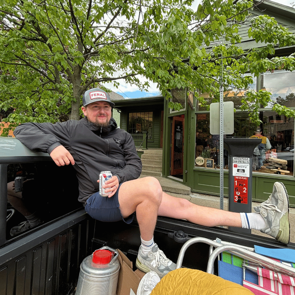 Charlie relaxes in a truck bed, drinking a beer with his legs stretched out, outside of the store.