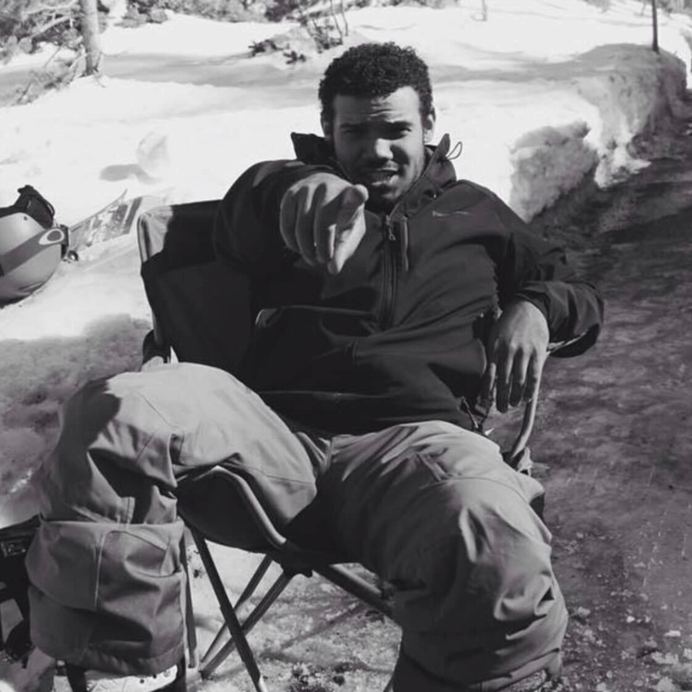 Jordan Haven, relaxed in a folding chair in the snow, points directly at the viewer, creating an engaging and personal connection.