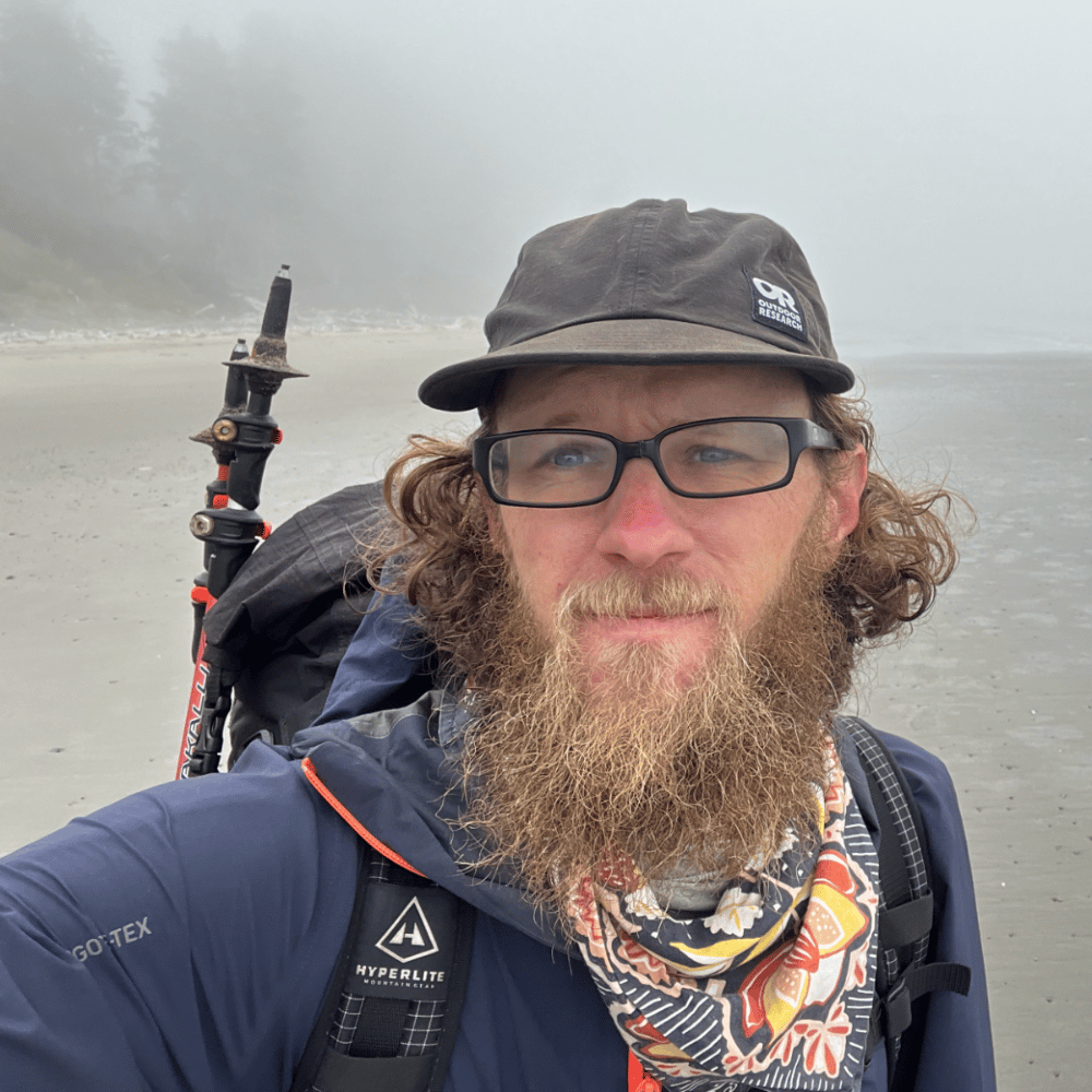 A reflective selfie of Josiah Cilladi on a misty beach, showcasing his backpacking gear and adventurous spirit.