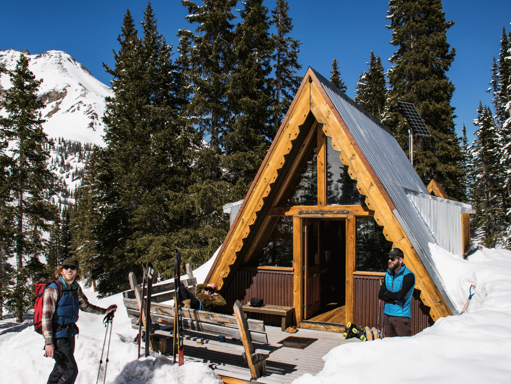 Snowy A-frame hut nestled in the mountains, inviting weary skiers for a cozy rest on their backcountry adventure.