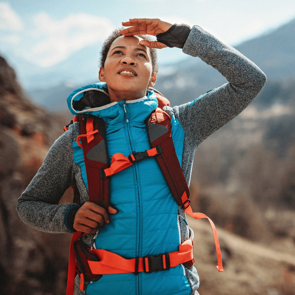 An adventurous hiker shields her eyes, wearing a bright blue backpack, evoking a sense of exploration.