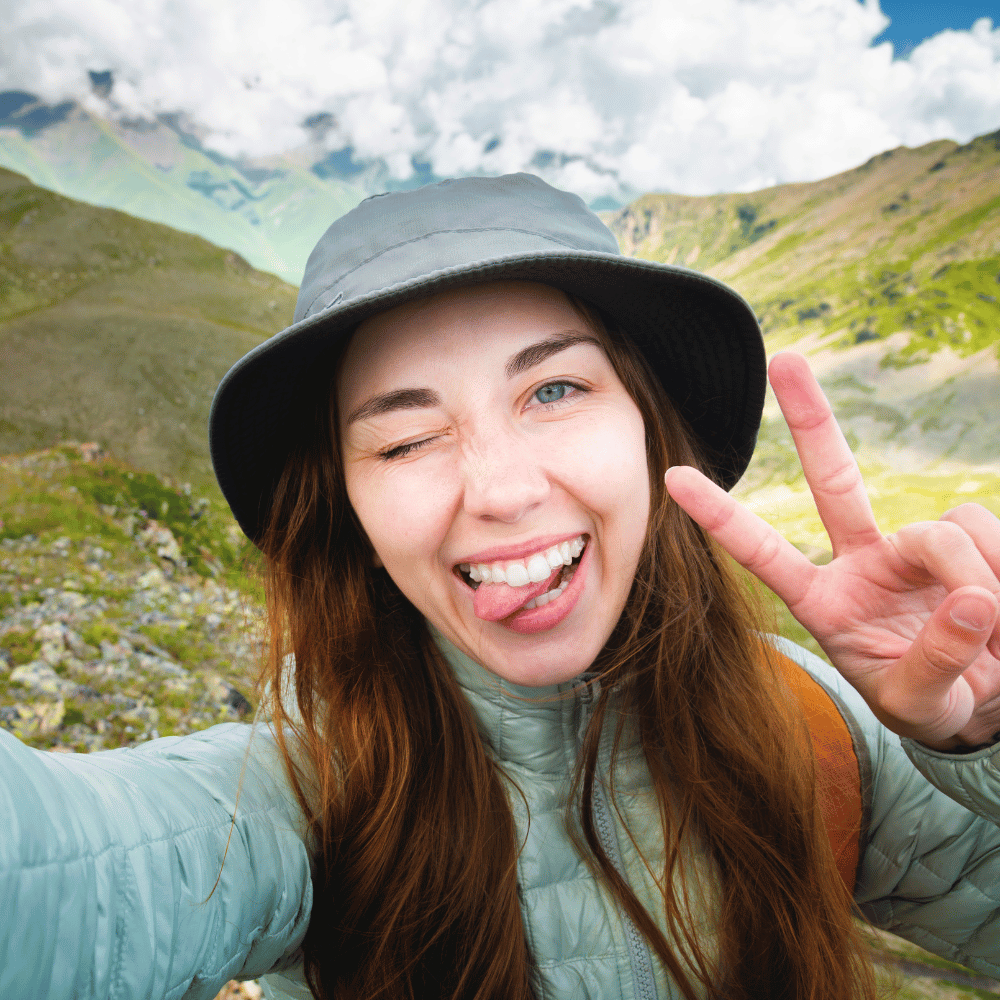 A carefree woman in outdoor apparel winks and flashes a peace sign against a mountain backdrop.