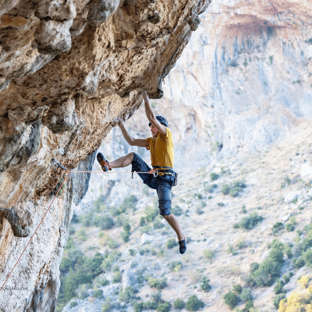 A rock climber in a yellow shirt scales a cliff, embodying the adventurous spirit of the Climb collection.