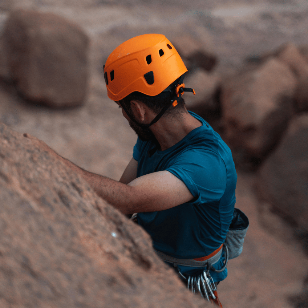 A rock climber in a yellow shirt scales a cliff.