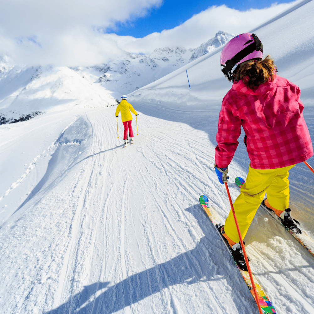 Two kids skiing down a snowy mountain; winter apparel in vibrant colors suggests an active, fun-filled lifestyle.