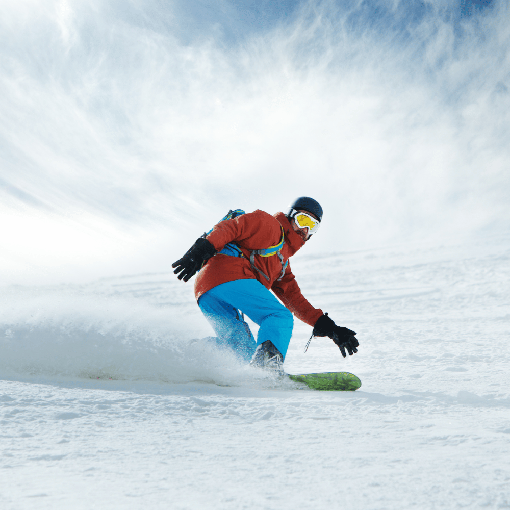 Person snowboarding down a snowy slope with a blue sky and clouds in the background