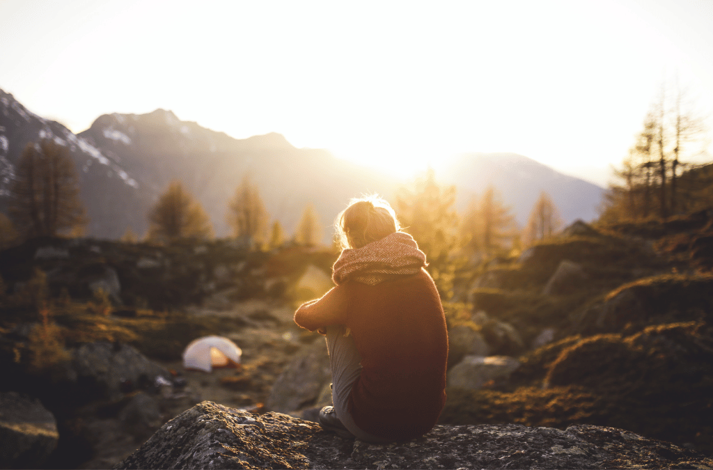 A lone figure sits atop a mountain rock, contemplating the vista at sunset, evoking a sense of serene reflection and the need to protect our natural spaces. 
