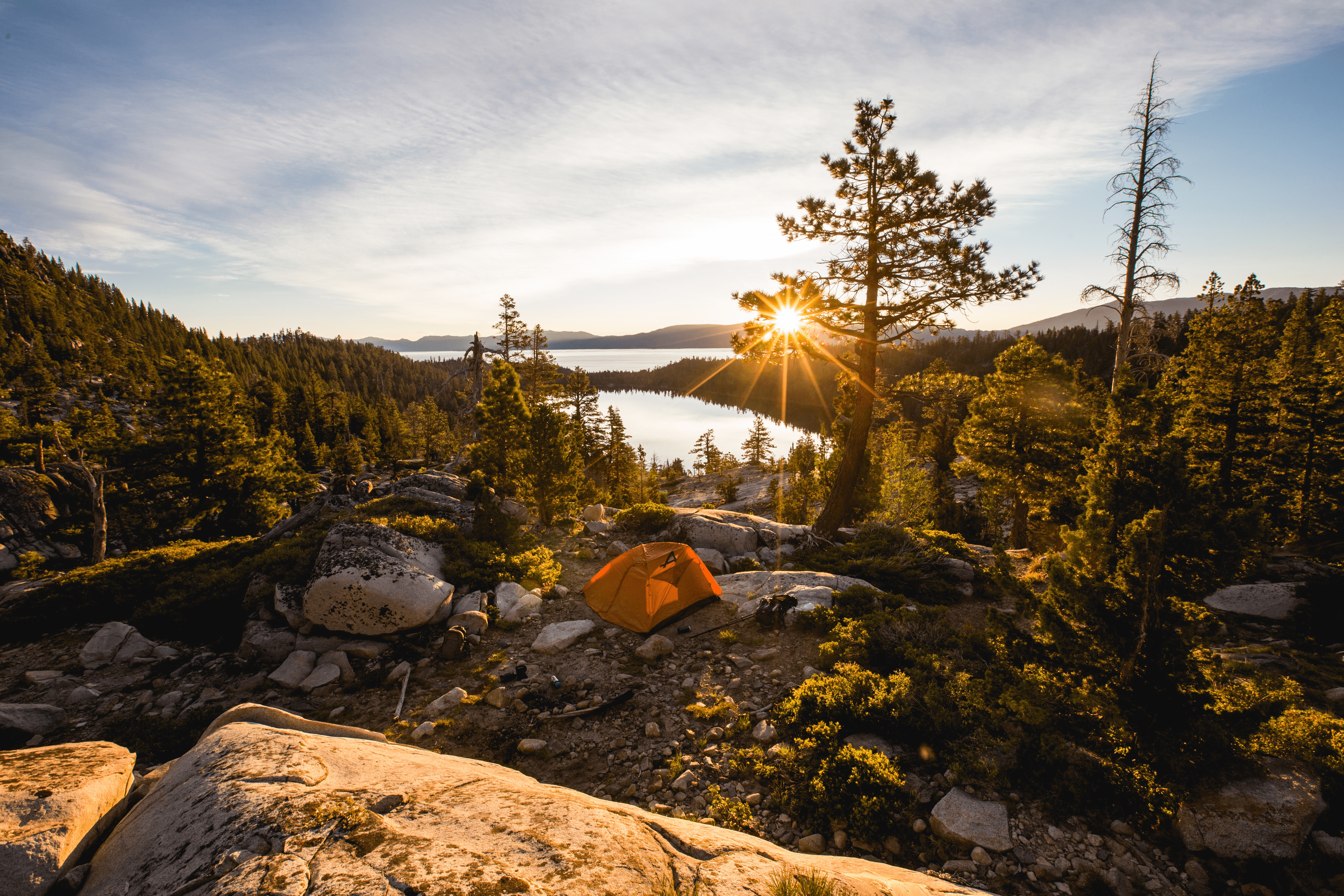 Golden sunlight illuminates a cozy orange tent pitched near a tranquil lake, evoking a peaceful camping escape in nature.

