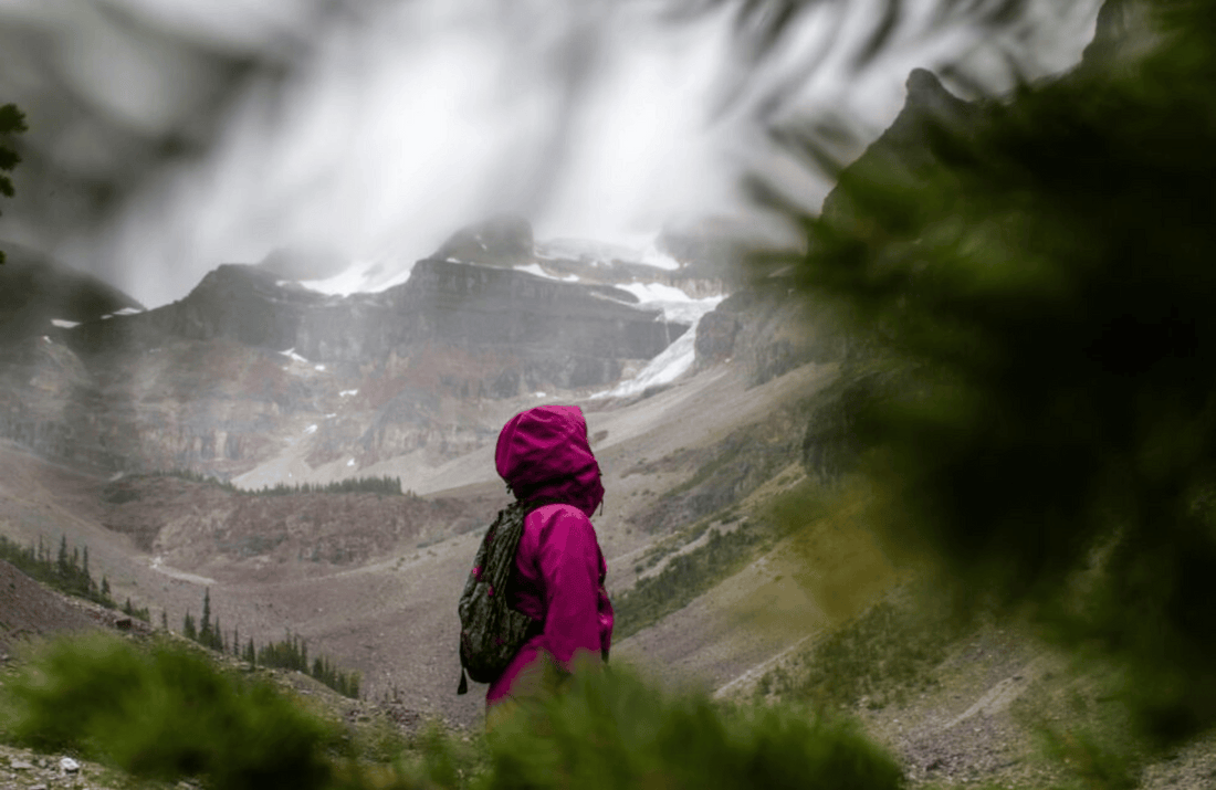 A lone hiker in a magenta jacket gazes at a majestic, misty mountain range, evoking a sense of adventure and awe.
