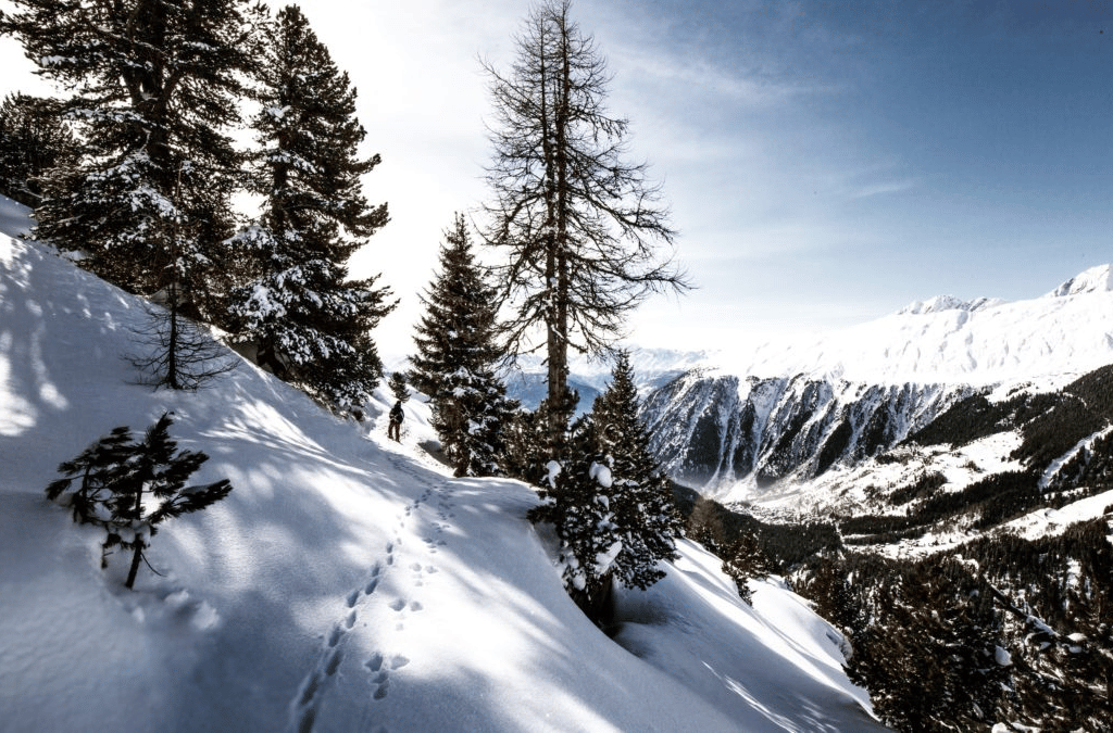 A lone snowshoer trudges through a snowy alpine landscape, evoking a sense of peaceful solitude in the mountains.
