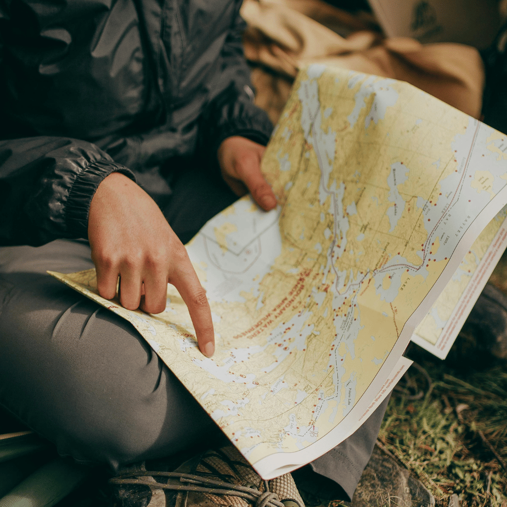 Person reading a detailed map outdoors; earthy tones, adventure theme, suggesting exploration and outdoor guides.
