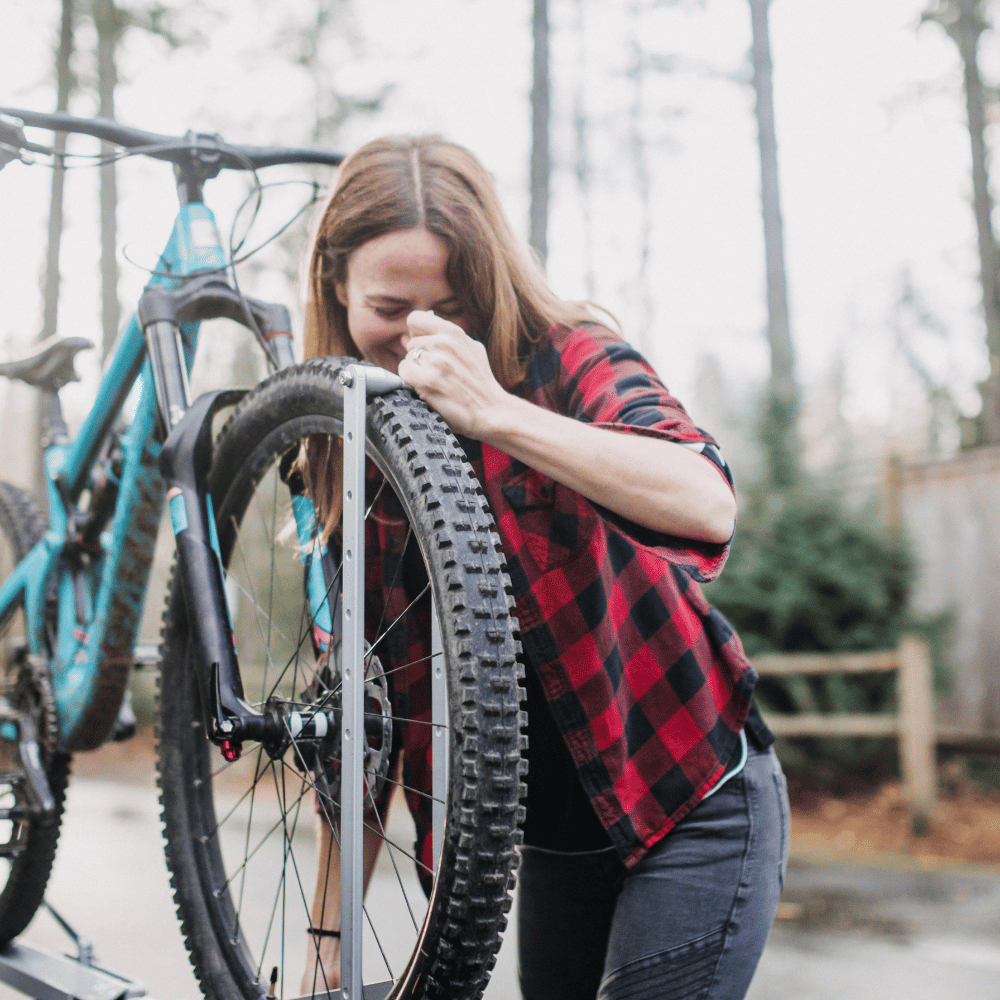 Woman adjusting a bicycle tire outdoors with trees in the background
