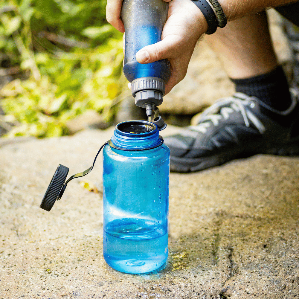 A person refills a translucent blue water bottle from a flexible water pouch outdoors.
