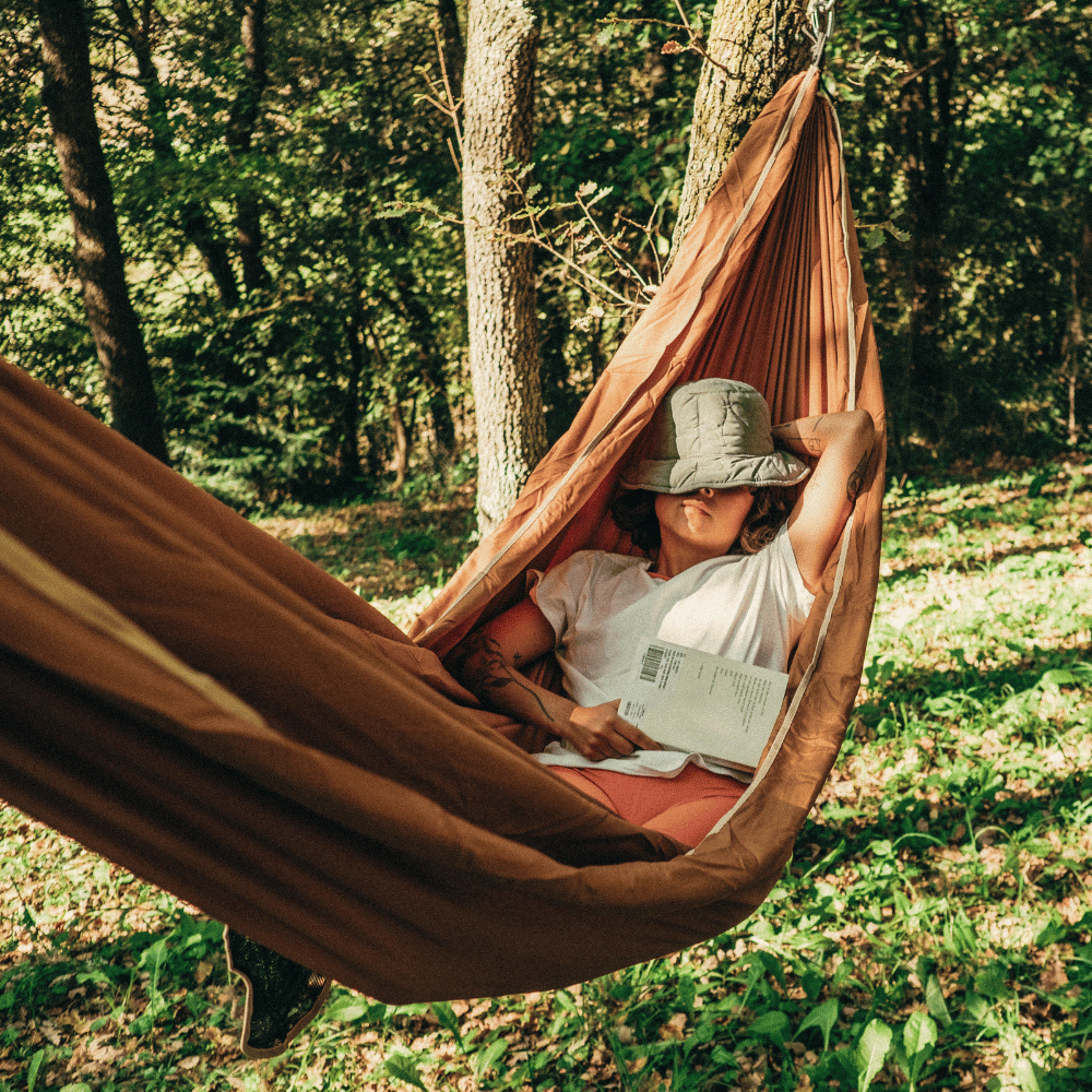 Person relaxing in a brown hammock outdoors. This is camping furniture to help you relax.
