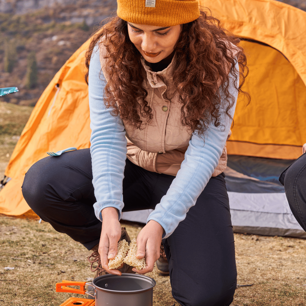 A woman prepares a camp meal by a tent; outdoorsy, practical camp kitchen collection.
