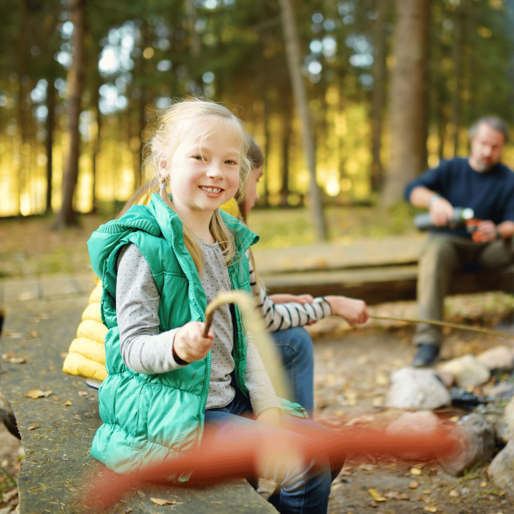 Child in a green vest sitting by a campfire in a forest with a blurred background