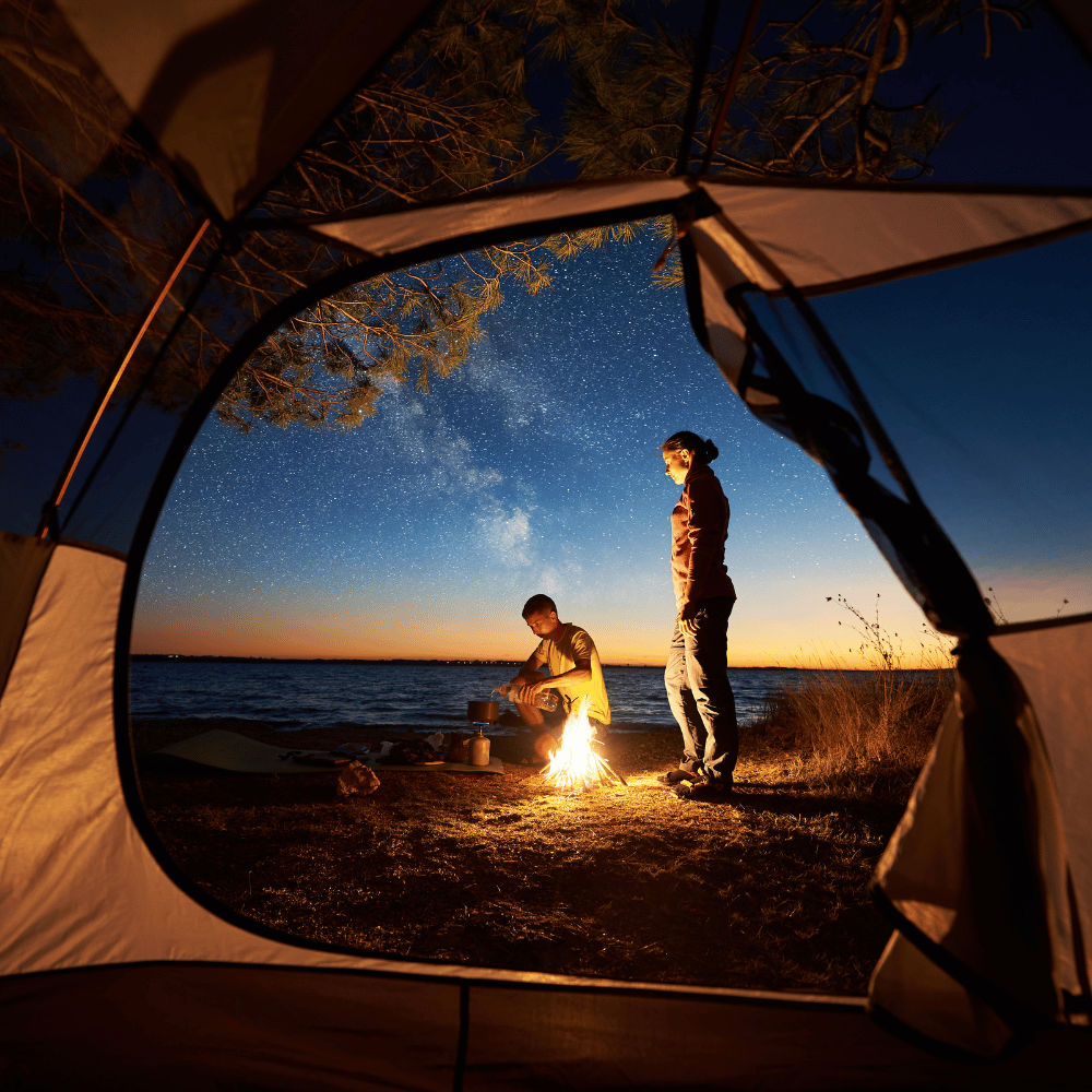 Camping tent view of two people by a campfire under a starry night sky, evoking adventure and the outdoors.
