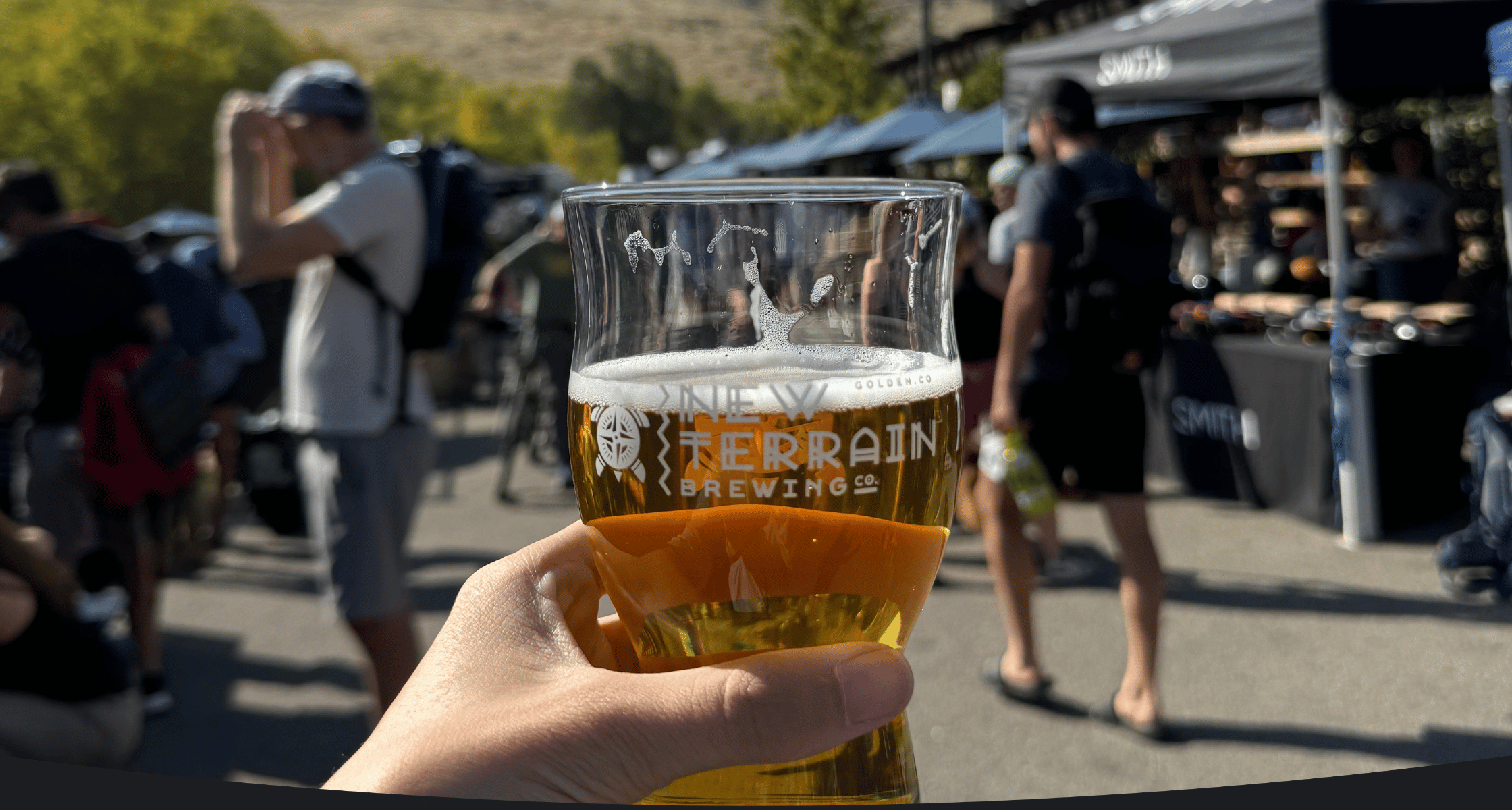 Hand holding a glass of beer with 'New Terrain Brewing' branding at an outdoor event.