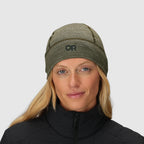 Olive green merino wool beanie by Outdoor Research, worn by a blonde woman with a black jacket.