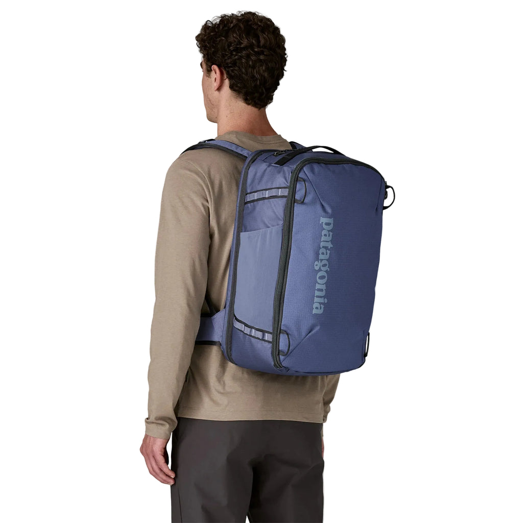 Blue backpack by Patagonia with a dark grey logo, worn by a man wearing a tan shirt and dark pants.