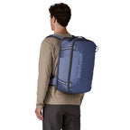 Blue backpack by Patagonia with a dark grey logo, worn by a man wearing a tan shirt and dark pants.