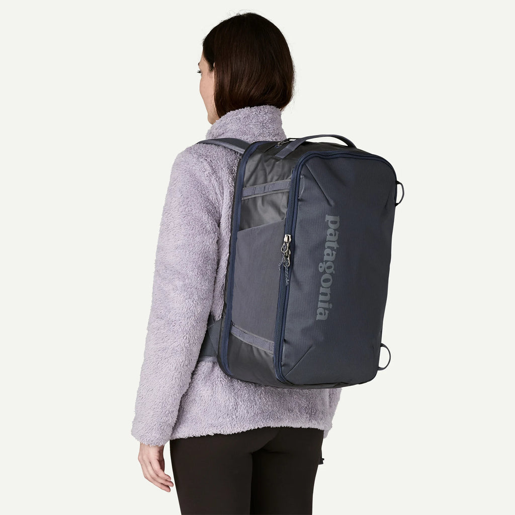 Navy carry-on backpack by Patagonia, shown on a person with a lilac fleece jacket and black leggings.
