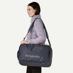 Navy blue convertible travel backpack by Patagonia, shown in a lifestyle shot, worn with a light purple fleece jacket.