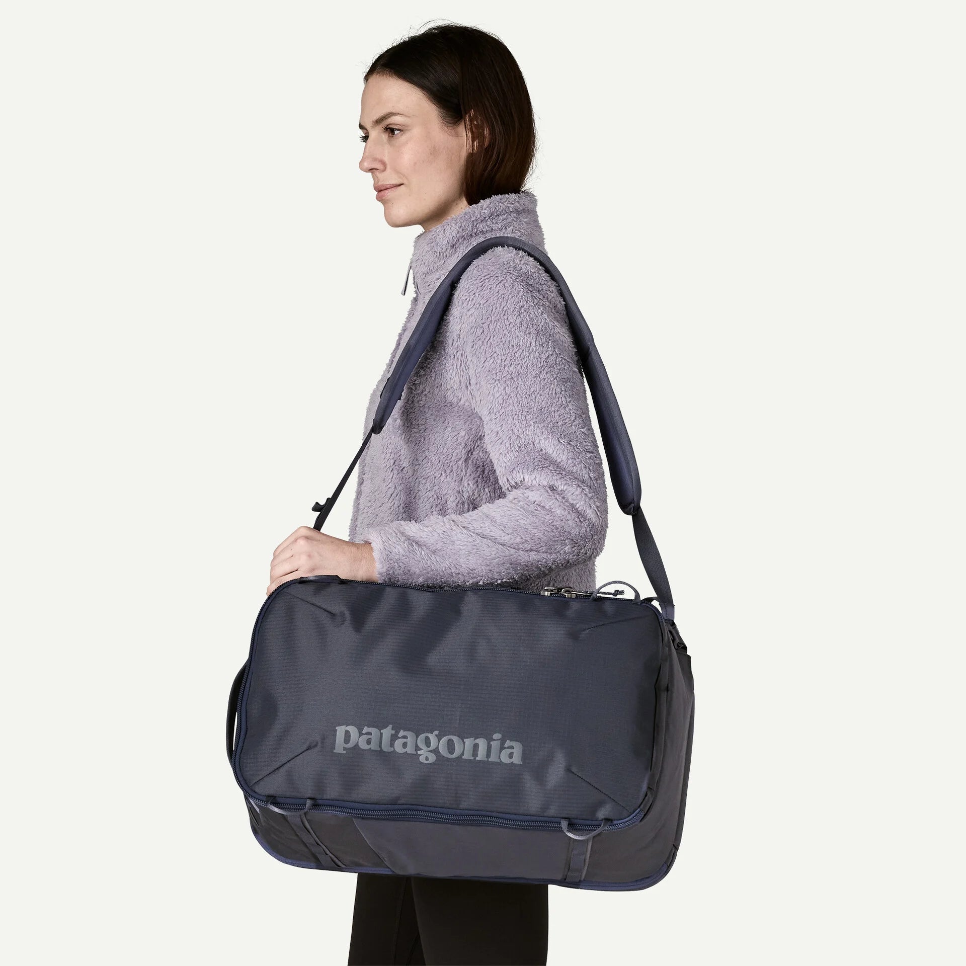 Navy blue convertible travel backpack by Patagonia, shown in a lifestyle shot, worn with a light purple fleece jacket.