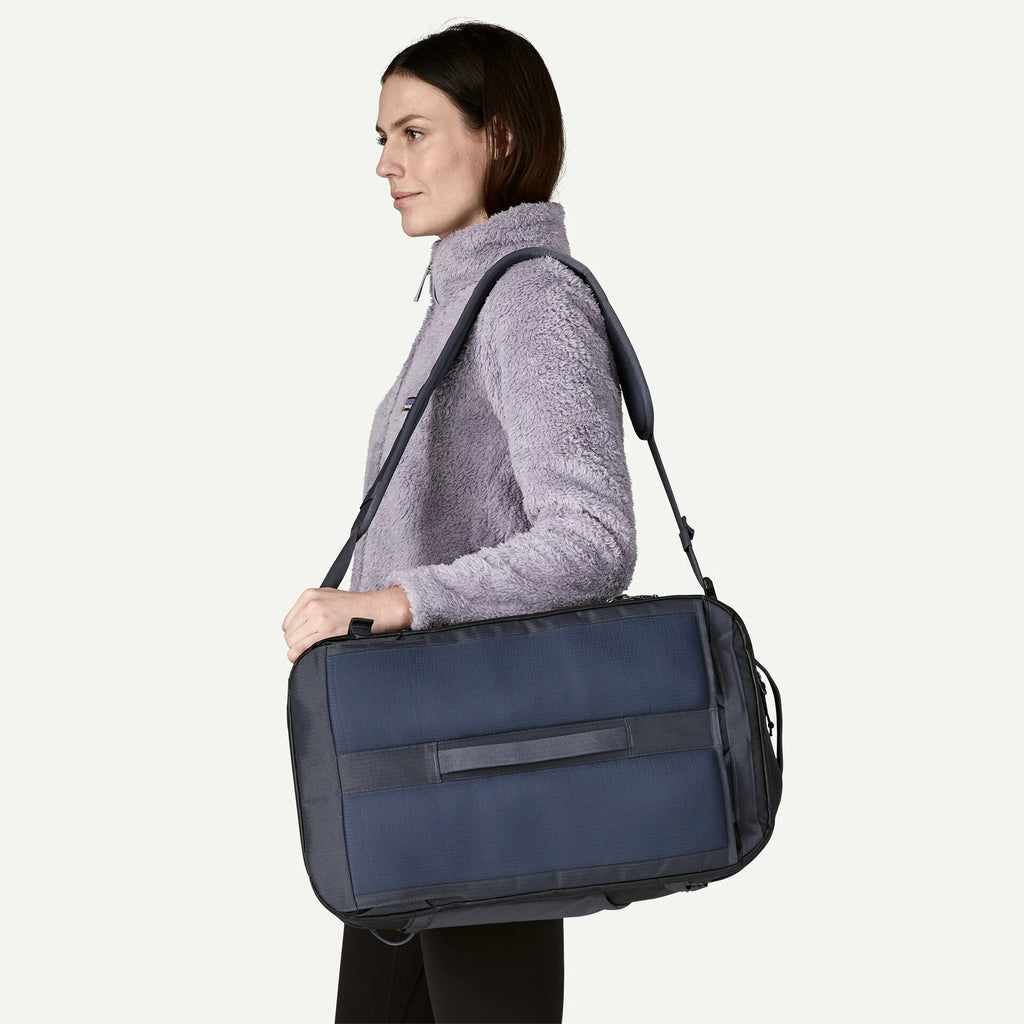 Blue backpack by Patagonia, slung over the shoulder, worn with a lavender fleece top.
