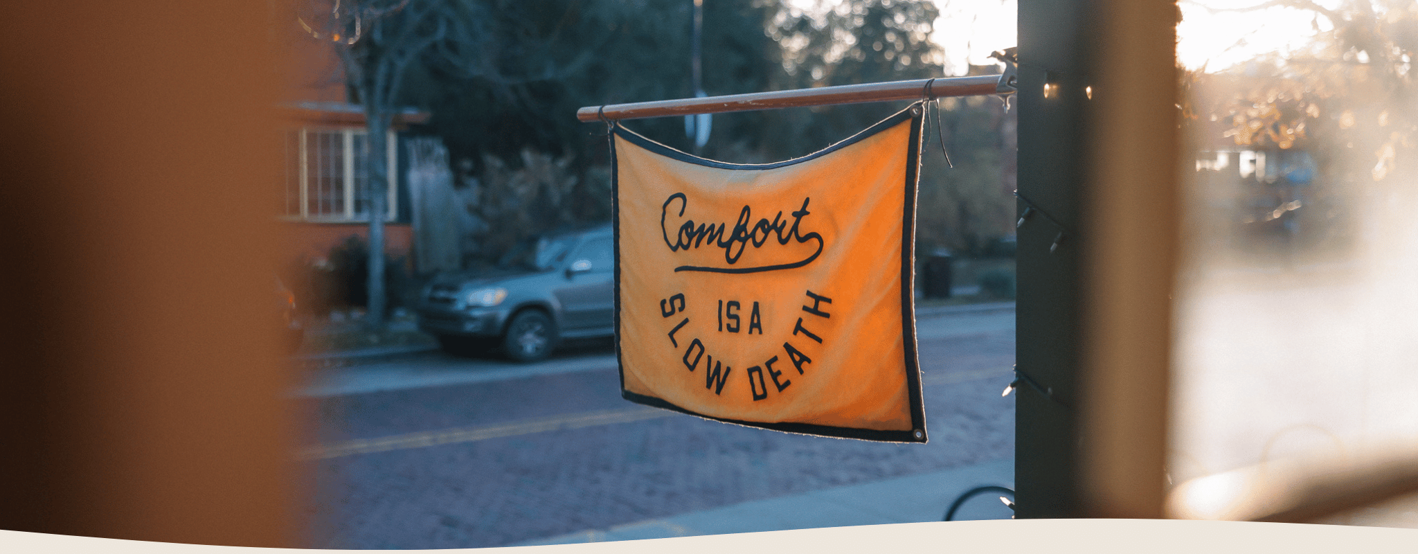 Flag with text 'Comfort is a Slow Death' hanging outside FERAL's front porch.