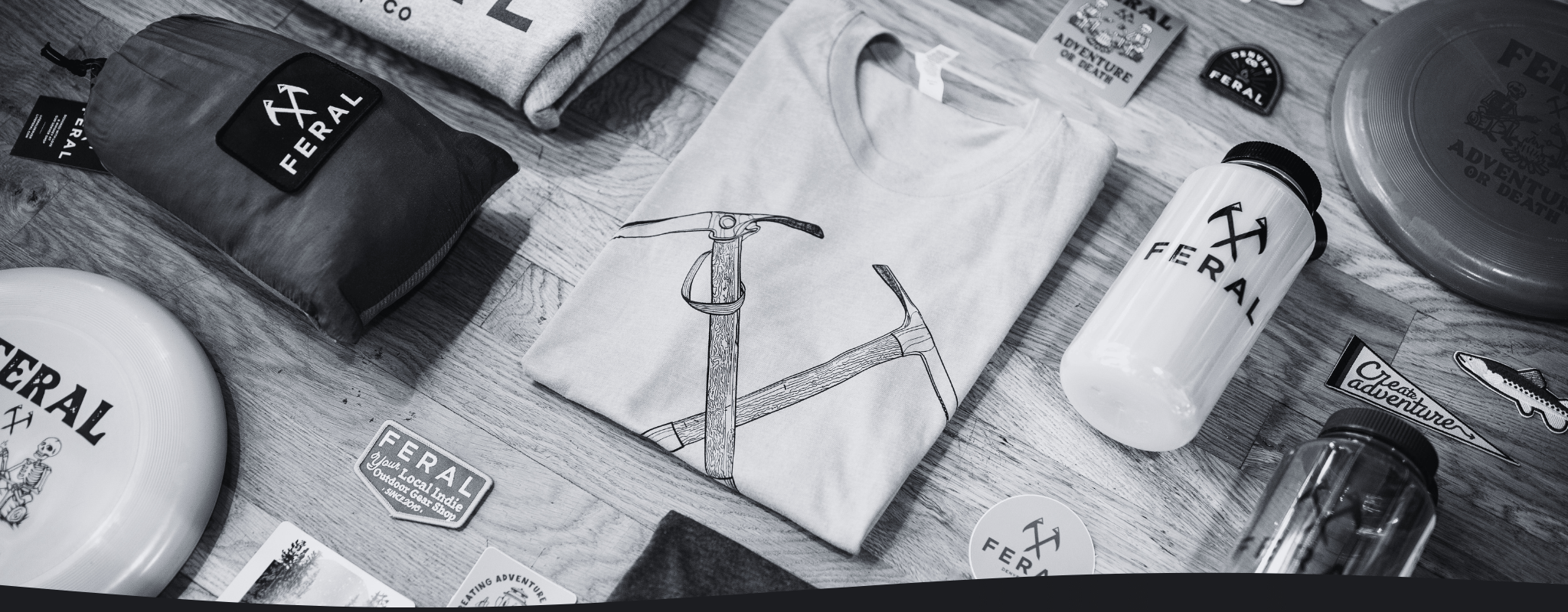 Collection of Feral brand products including hats, a t-shirt and bottles on a wooden surface.