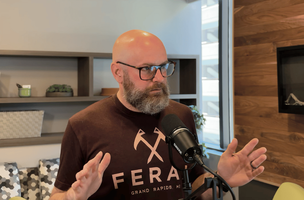 Jimmy Funkhouser wearing a brown 'FERAL' t-shirt speaking into a microphone.