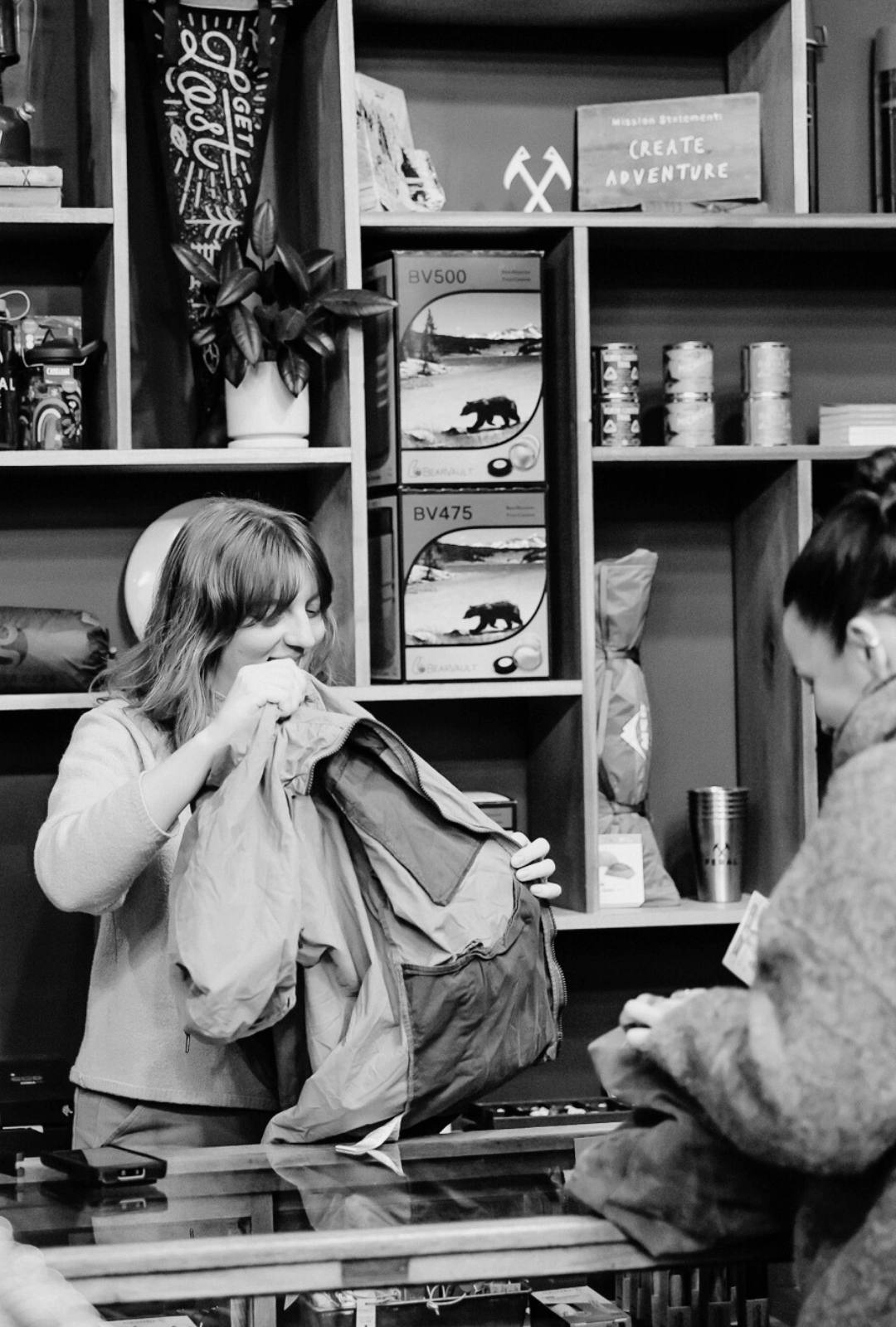 Two people at a checkout counter with shelves filled with outdoor gear and decorative items.