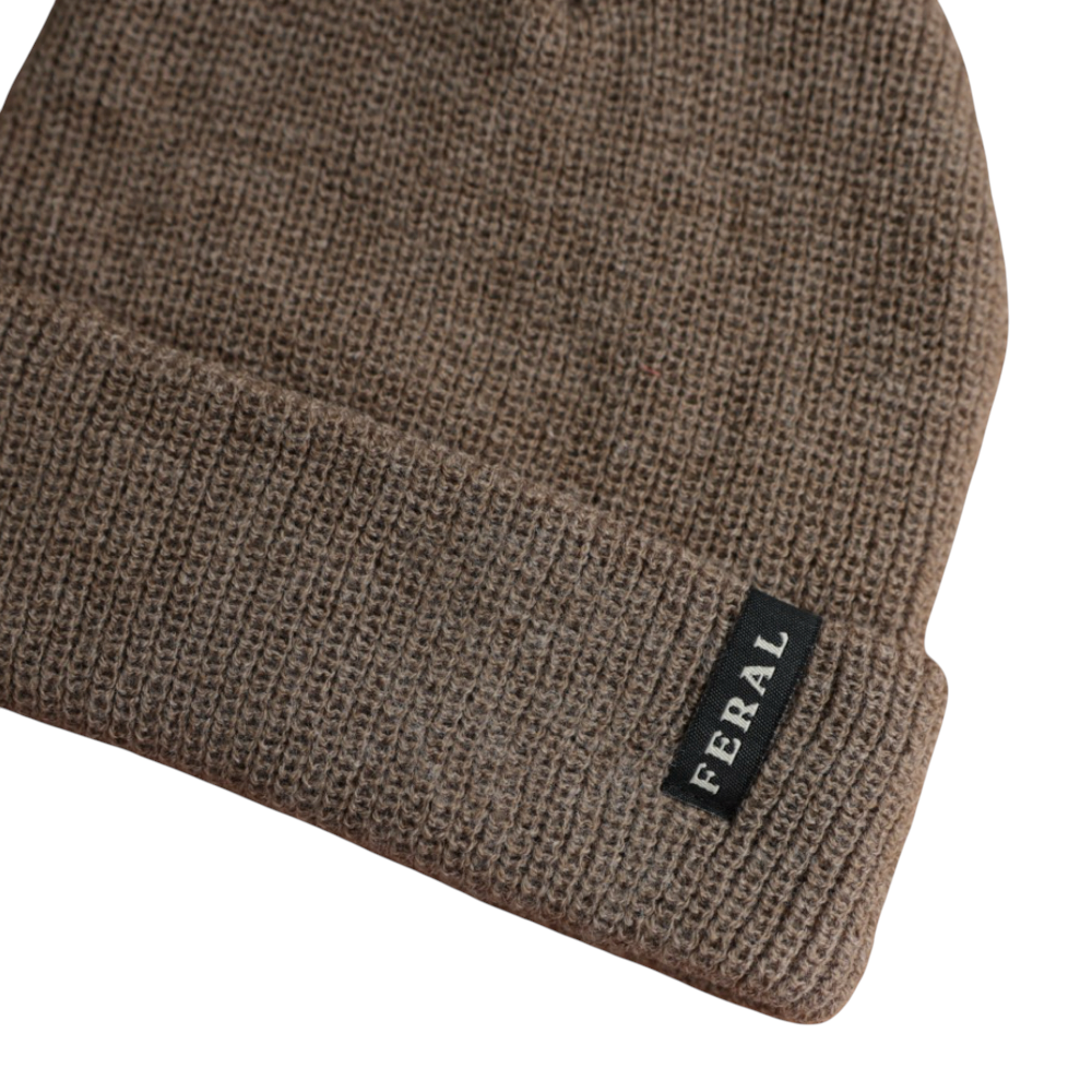 Brown knit beanie by FERAL, showing a folded brim with a small rectangular logo tag.