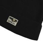 Black knit beanie by FERAL featuring a woven logo patch with a mountain landscape graphic.
