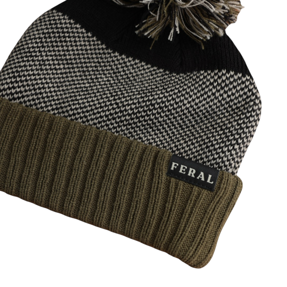 Knit beanie by FERAL with black and white patterned crown and olive ribbed brim, topped with a pompom.