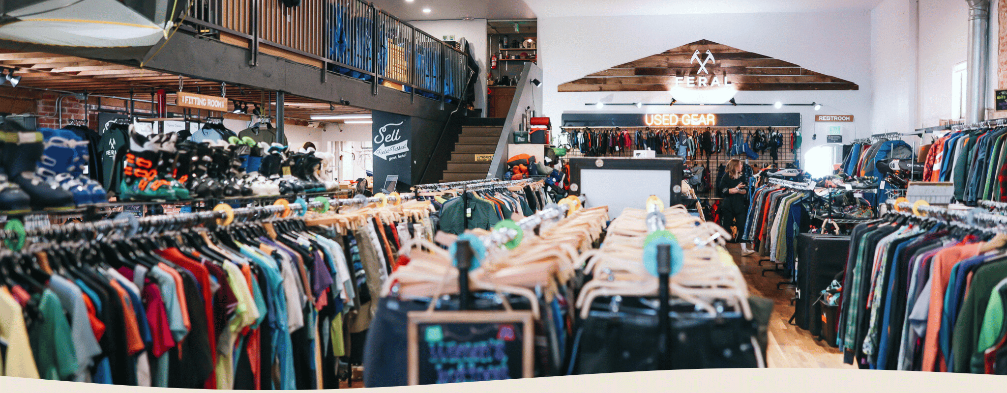 Interior of a clothing store with racks of clothes and a staircase in the background.