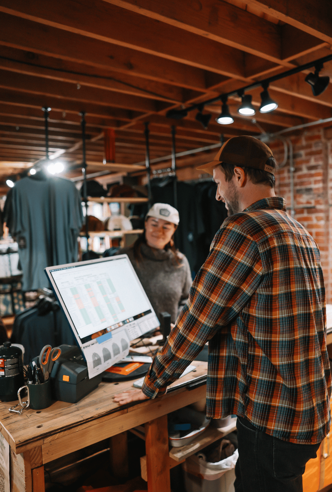 Two people working at a counter in a rustic store setting with a computer screen displaying a graph.