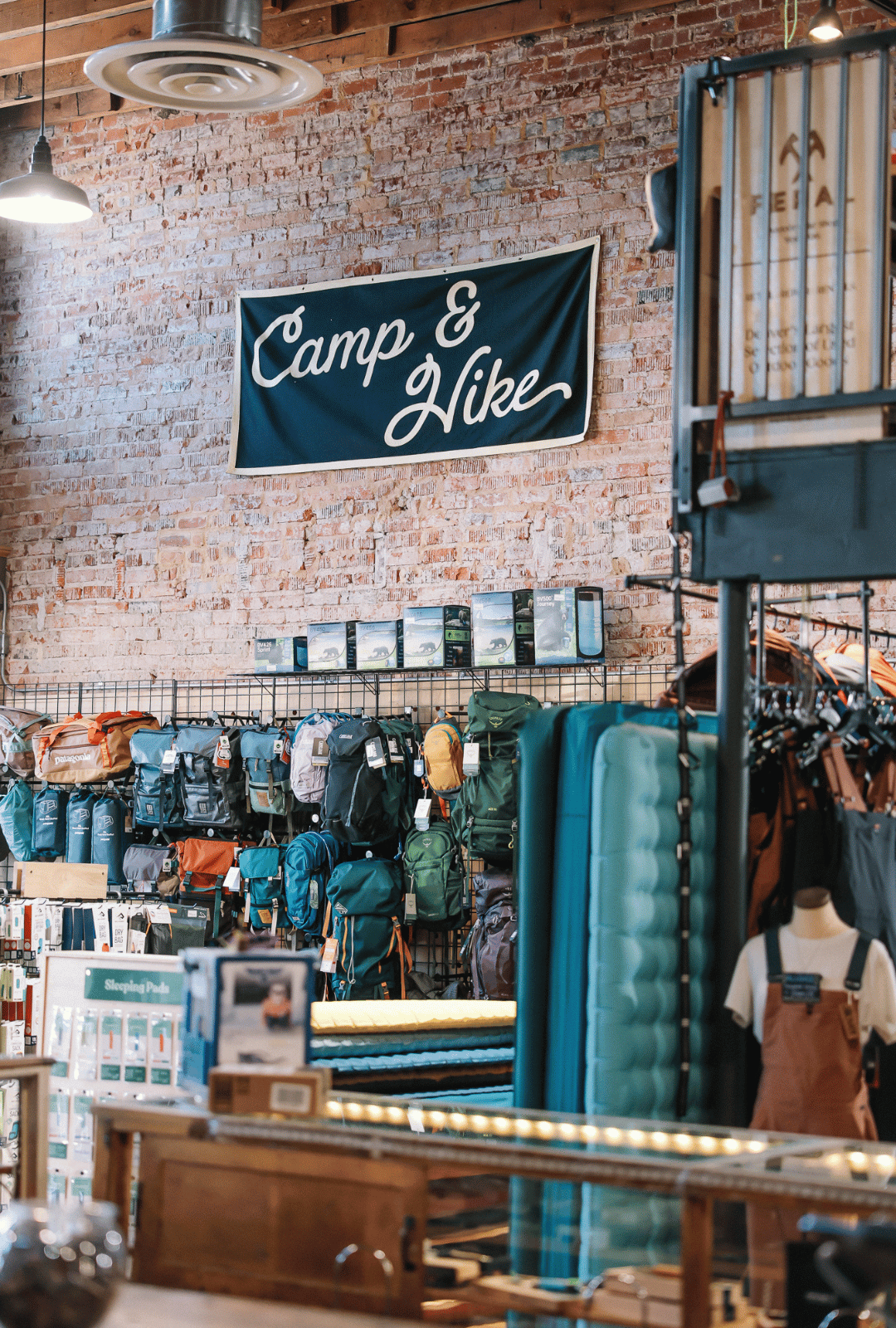 Store interior with 'Camp & Hike' banner on brick wall, displaying outdoor gear.