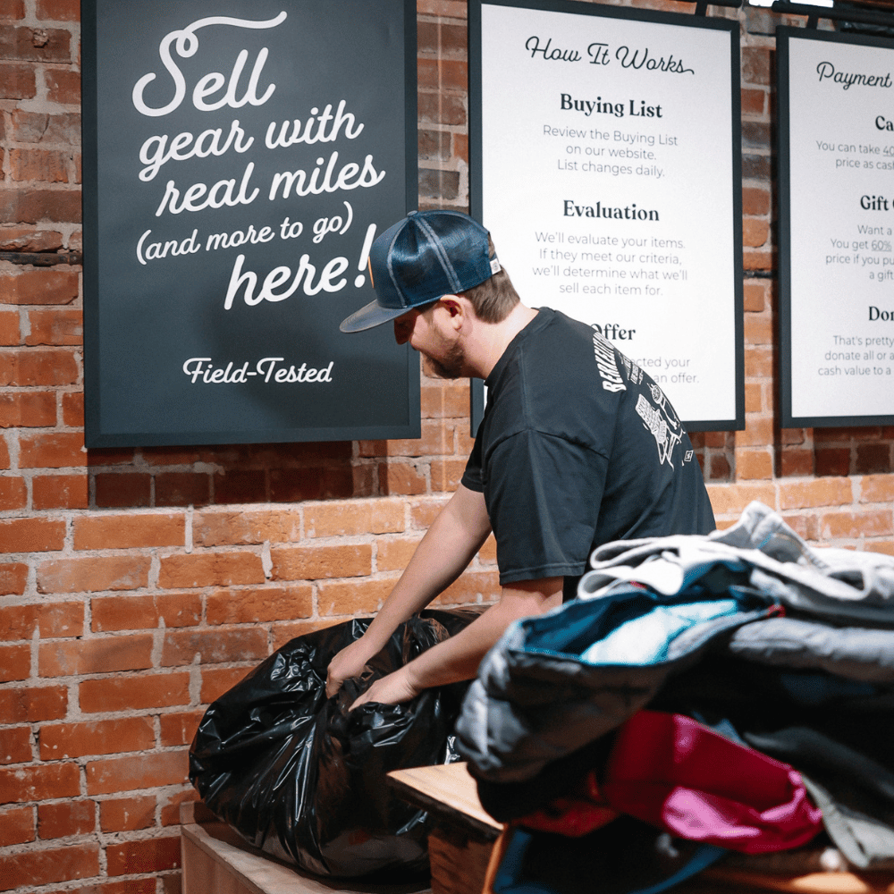 Person sorting through items next to a brick wall with signs about selling used gear.