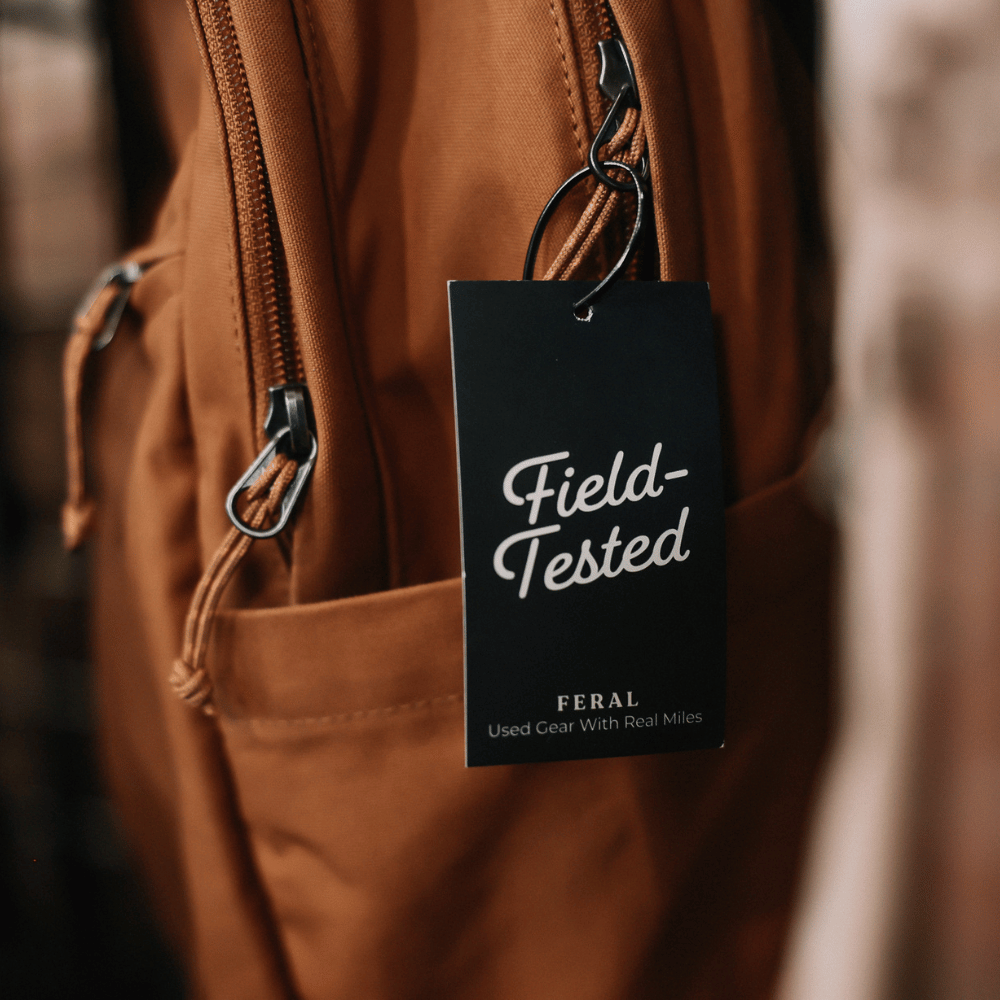 Brown backpack with a 'Field-Tested' tag by FERAL on a blurred background