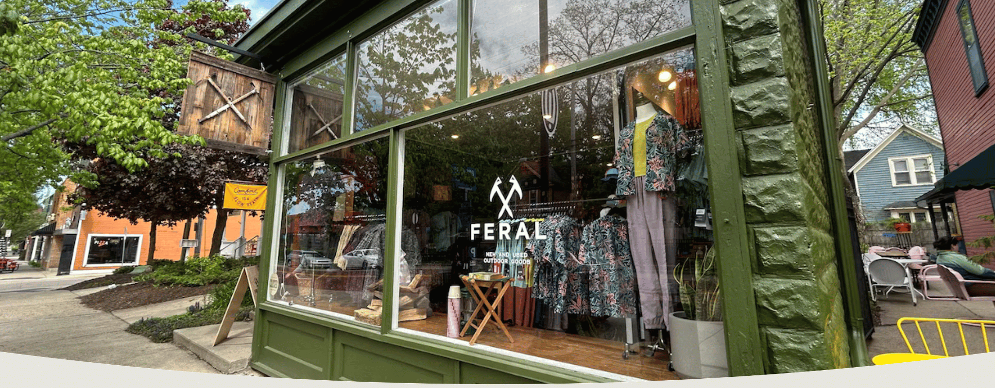 Storefront with 'Feral' clothing display, surrounded by trees and a sidewalk.