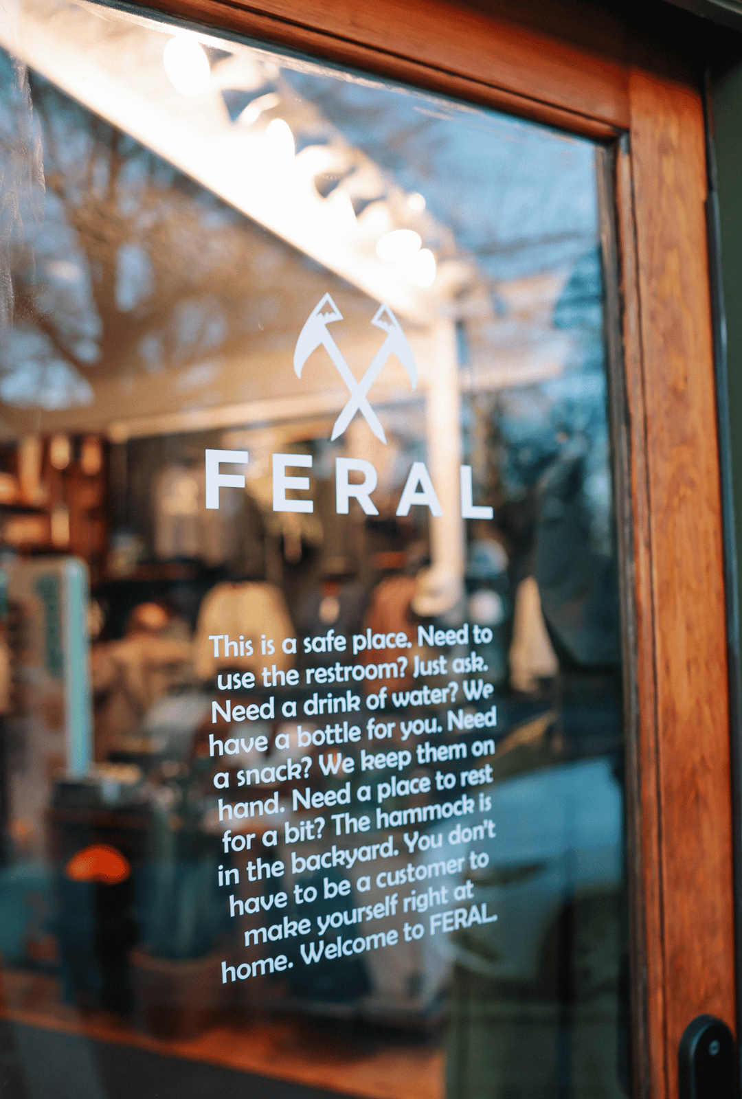Glass door with 'FERAL' branding and welcoming message inside a building.