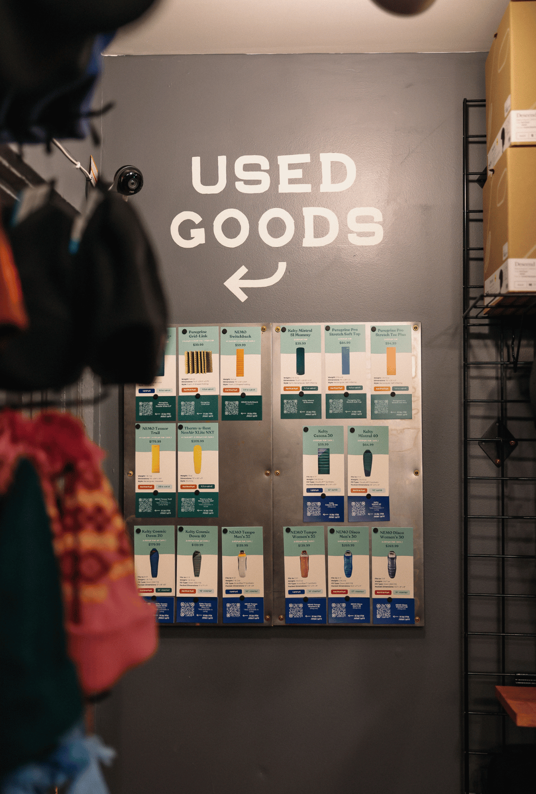 Store interior with 'Used Goods' sign and product display on a gray wall.
