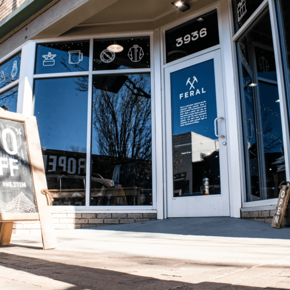 Exterior view of FERAL store. White-framed glass door and windows display logos and text. 
