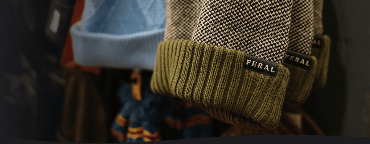 Green and tan beanie with a FERAL tag hanging in a retail shop.