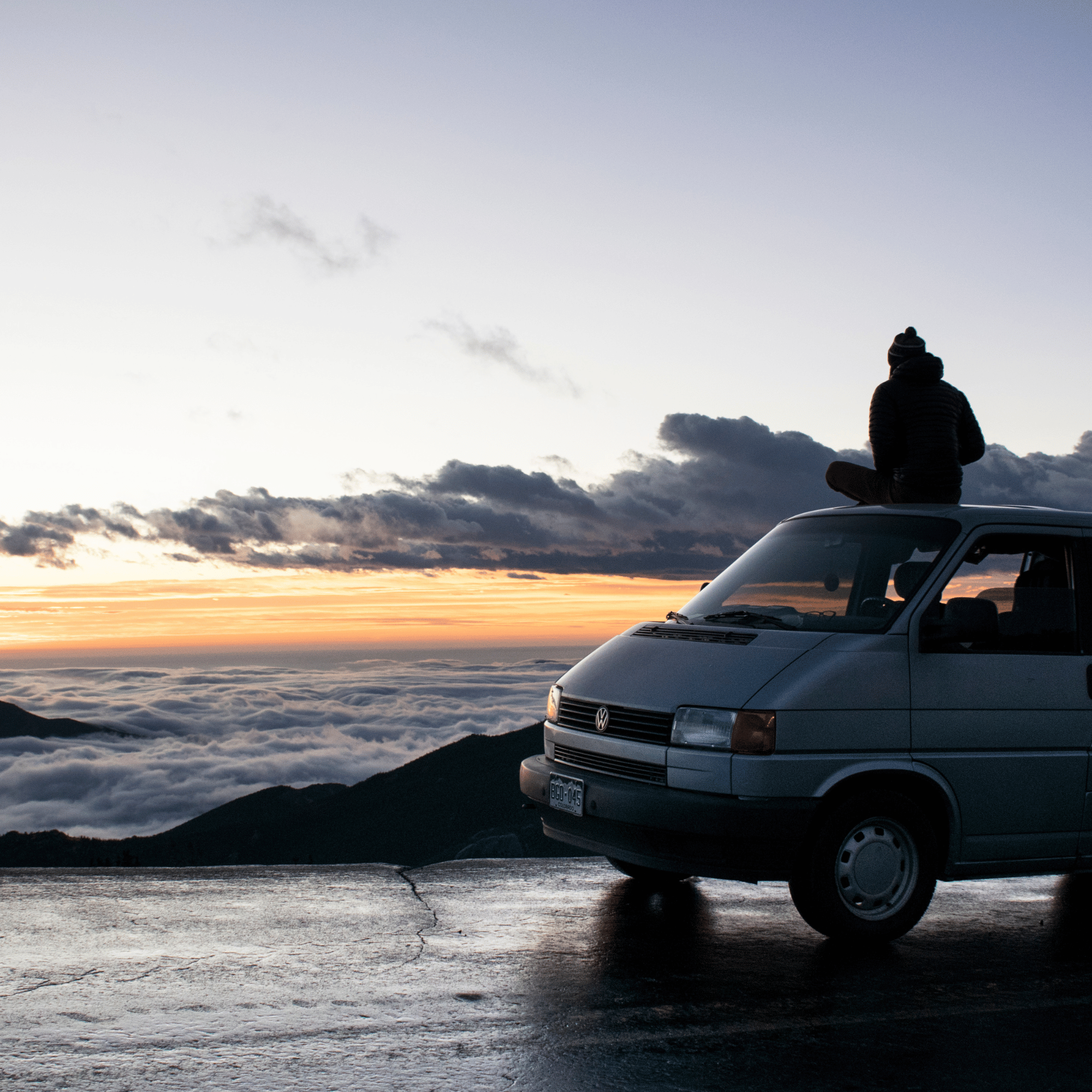 Person sitting on a van with a scenic view of clouds and sunset.