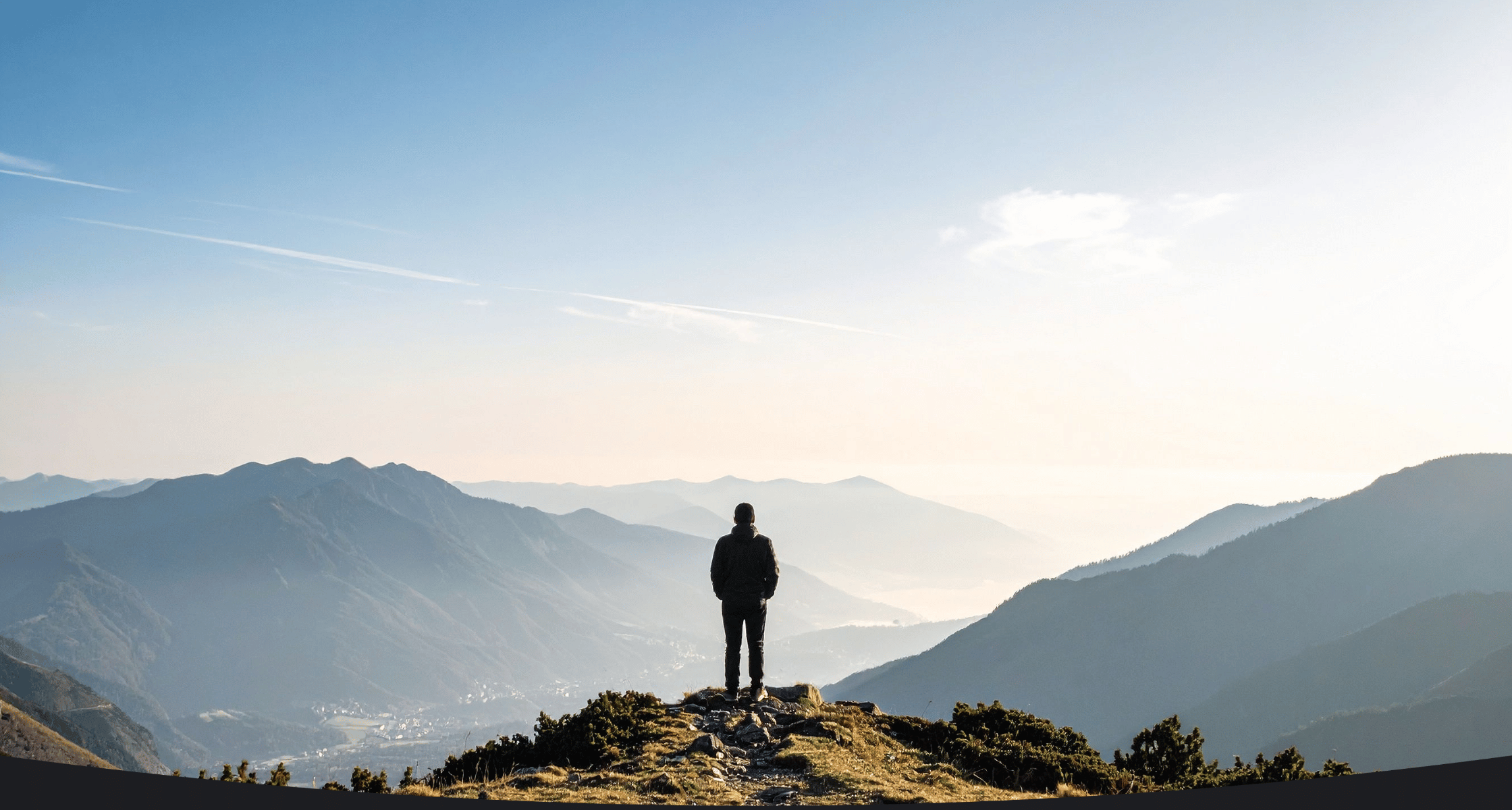 Person standing on a mountain peak with a vast landscape in the background