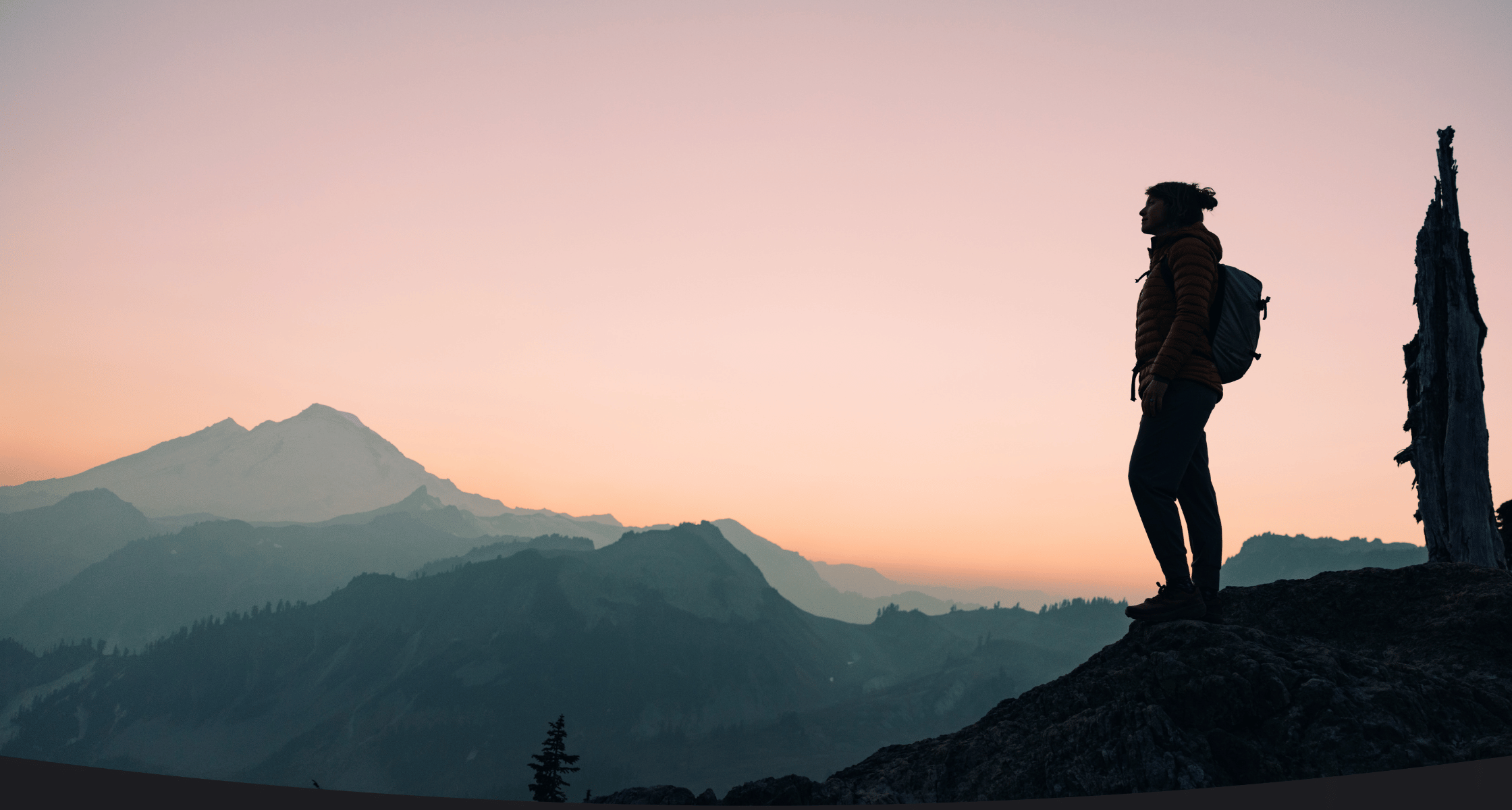 Silhouette of a person with a backpack standing on a mountain at sunset.