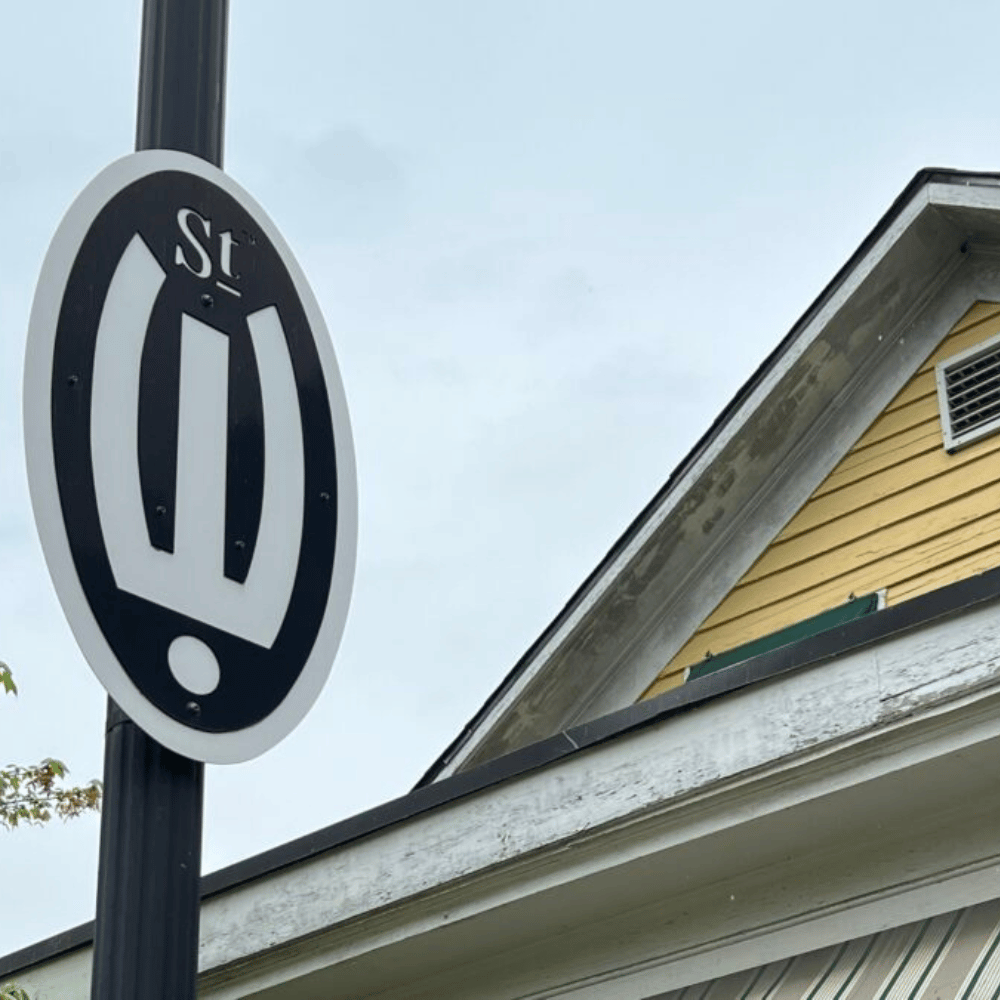 Street sign with a black oval on a pole with "St" above a white horseshoe shape.